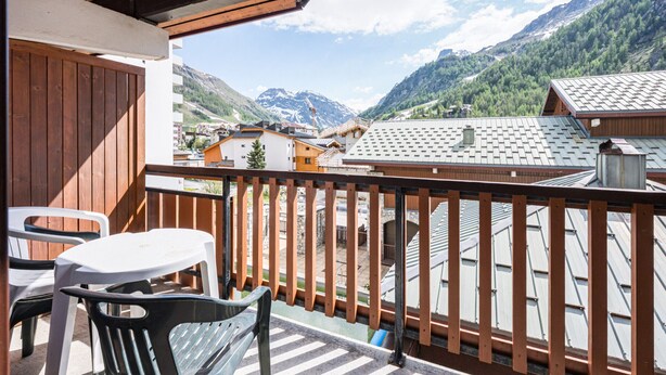 A balcony with a view of a mountainous landscape, wooden railings, and a table with chairs.