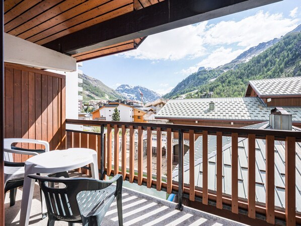 Ein Balkon mit Blick auf eine Berglandschaft, Holzgeländern und einem Tisch mit Stühlen.
