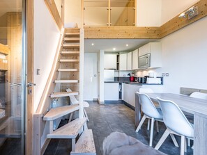Una cocina moderna con una escalera de madera, sillas blancas y una mesa de comedor.