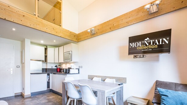 A modern kitchen with white cabinets, a dining table with chairs, and a sign for 'Mountain Collection Immobilier' on the wall. - Renovated Studio with Mezzanine – Val-d'Isère Center (Val-d'Isère)