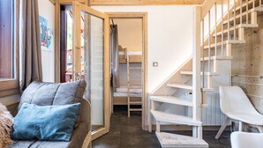 A cozy room with a wooden staircase, a bunk bed, a sofa with cushions, and a white chair. - Renovated Studio with Mezzanine – Val-d'Isère Center (Val-d'Isère)