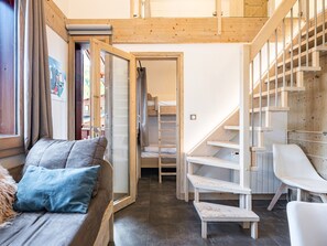 Quarto aconchegante com escada de madeira, beliche, sofá com almofadas e uma cadeira branca.