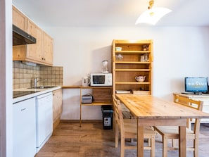 A compact kitchen with wooden cabinets, a microwave, a coffee maker, and a television displaying 'MOUNTAIN collection'.