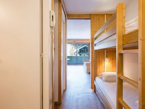 A narrow hallway with wooden bunk beds, a telephone, and a view of an outdoor area with a bench.