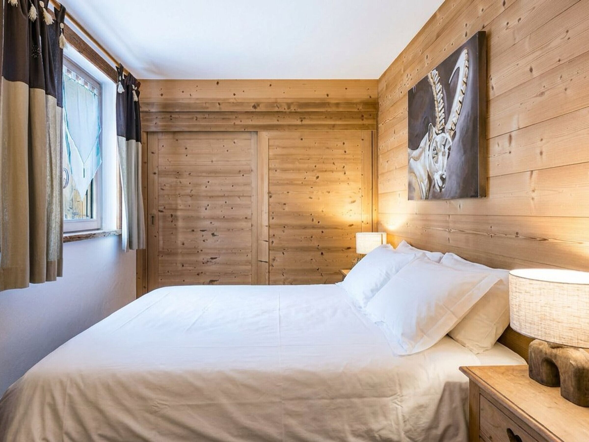 A wooden-paneled room with a bed, a nightstand, and a painting on the wall.