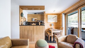 A modern interior with a wooden dining area, a kitchen with wooden cabinets, and a large window offering a view.