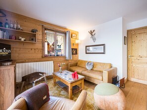 Un salon chaleureux avec un canapé, un fauteuil et une table basse, des murs en bois, une tête de cerf accrochée au mur et une fenêtre avec des rideaux.