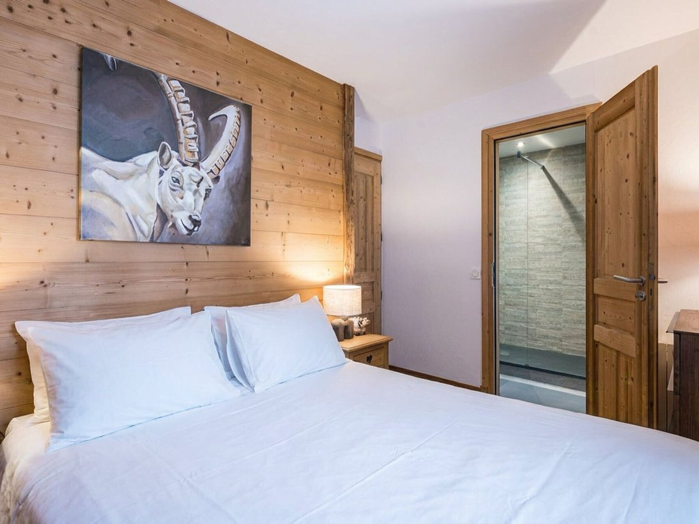 A bedroom with a wooden headboard, a bed with white linens, a painting of a cow, and a wooden door.