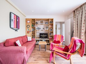 Ein Wohnzimmer mit einem roten Sofa, einem Fernseher, einem hölzernen Bücherregal und einem gestreiften Sessel.