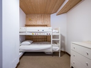 Quarto com beliche, teto de madeira, cômoda branca e piso coberto por carpete.