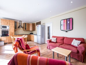 A modern kitchen with wooden cabinets, a refrigerator, and a dining area with a striped chair and a red sofa.
