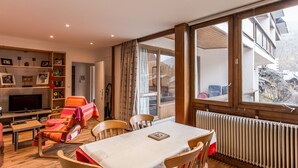 A cozy living room with a dining table, chairs, a TV, and a bookshelf. - Comfortable 3-room apt · Near center · 5 min from slopes · Parking · Wifi (Val-d'Isère)
