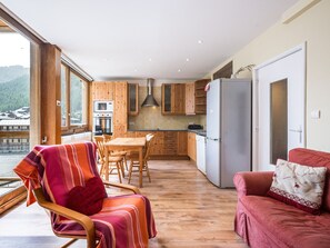 Cozinha moderna com armários de madeira, sala de jantar com mesa e cadeiras, e área de estar com sofá.