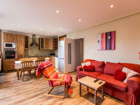 Un espacio habitable compacto con kitchenette, comedor y zona de estar con sofá y sillón.