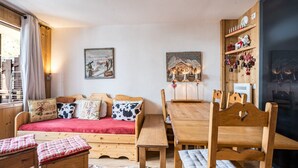A cozy room with a wooden sofa, a dining table, chairs, a cowhide rug, and wooden shelves with decorative items. - Cozy 2-room apartment in La Daille, 4 people, ski-in/ski-out (Val-d'Isère)
