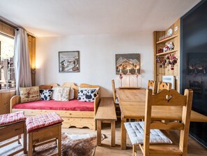 A cozy room with a wooden sofa, a dining table, chairs, a cowhide rug, and wooden shelves with decorative items.