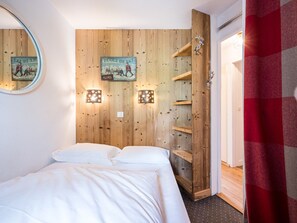 A bedroom with a wooden wall, a bed, a shelf unit, and a mirror.