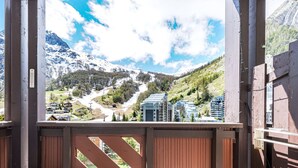 A wooden balcony with a view of a mountainous landscape, a chair, and a table. - Cozy 2-room apartment in La Daille, 4 people, ski-in/ski-out (Val-d'Isère)