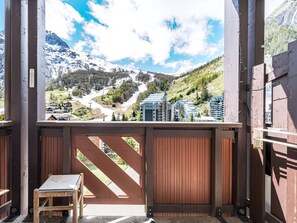 A wooden balcony with a view of a mountainous landscape, a chair, and a table.