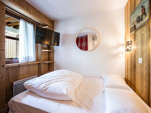 A bedroom with a bed, a mounted TV, a round mirror, and wooden walls.