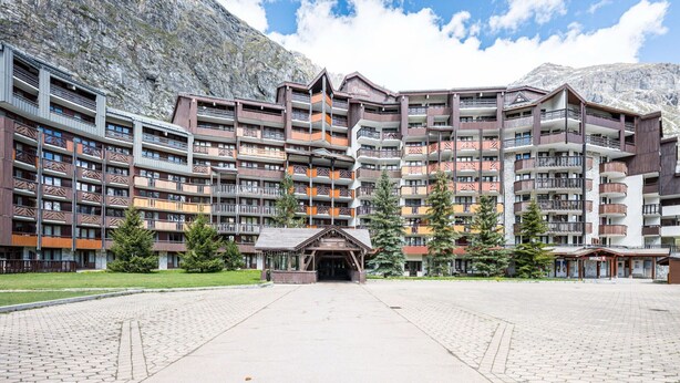 A multi-story hotel with balconies, a central entrance, and a mountainous backdrop. - Cozy 2-room apartment in La Daille, 4 people, ski-in/ski-out (Val-d'Isère)