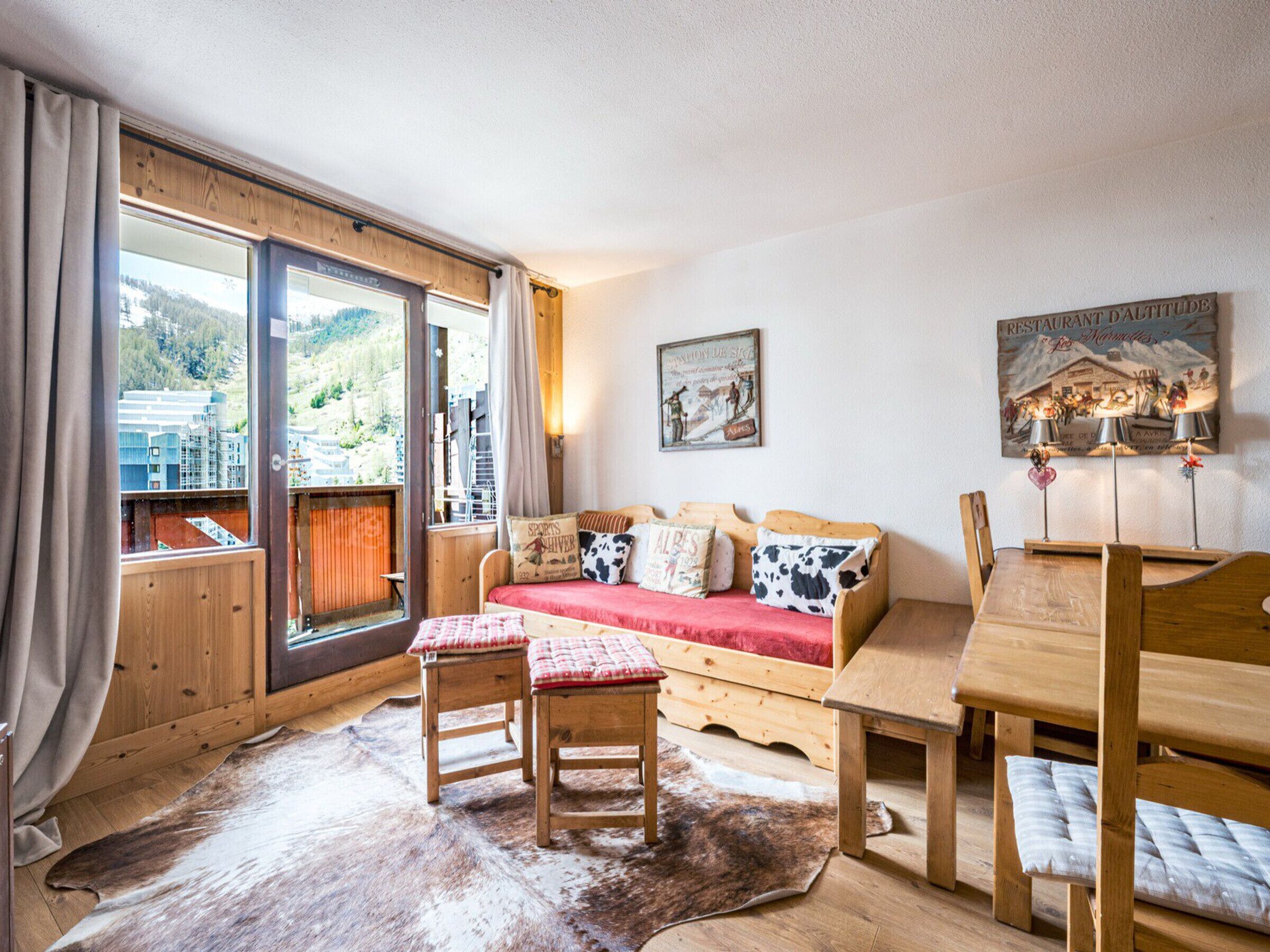 A cozy room with a wooden sofa, a dining table, and a large window with curtains.