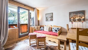A cozy room with a wooden sofa, a dining table, and a large window with curtains. - Cozy 2-room apartment in La Daille, 4 people, ski-in/ski-out (Val-d'Isère)