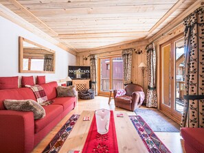 A cozy room with a red sofa, a wooden ceiling, a television, and a large window with curtains.