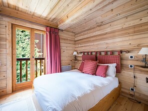 A wooden cabin bedroom with a bed, a window with curtains, a nightstand, and a lamp.