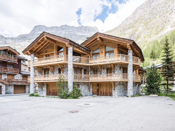 A multi-story wooden building with balconies, stone foundations, and a mountainous backdrop.