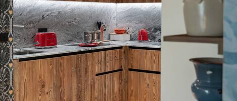 Una cocina con armarios de madera, encimera de mármol y hervidor rojo.