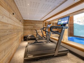 A gym with treadmills, stationary bikes, and a large window with a view of a mountainous landscape.