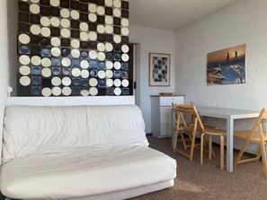 Uma sala de estar moderna com um sofá branco, uma mesa de jantar com cadeiras de madeira, um pequeno armário branco e uma parede decorada com espelhos redondos.