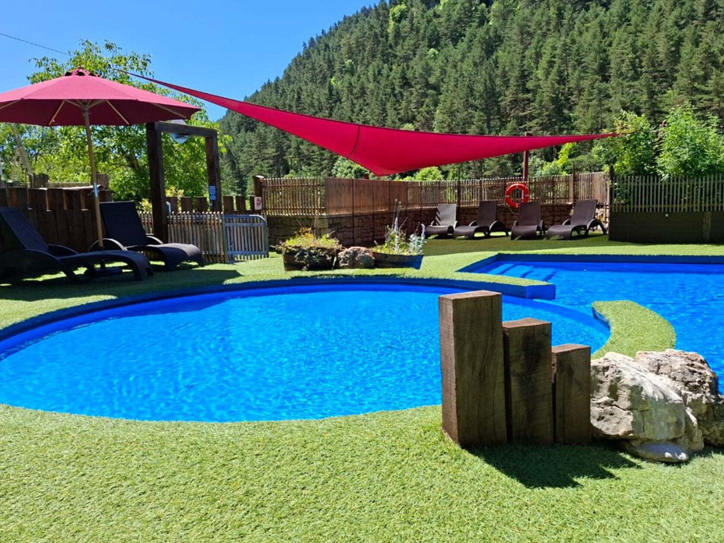 A backyard with a swimming pool, lounge chairs, and a wooden deck.