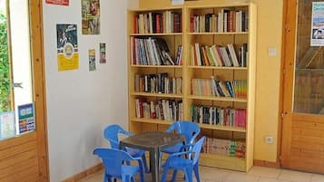 A small library with a wooden bookshelf, a round table, and blue chairs.