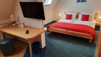 Una habitación de hotel con cama, escritorio con televisor, un basurero pequeño y ventana.