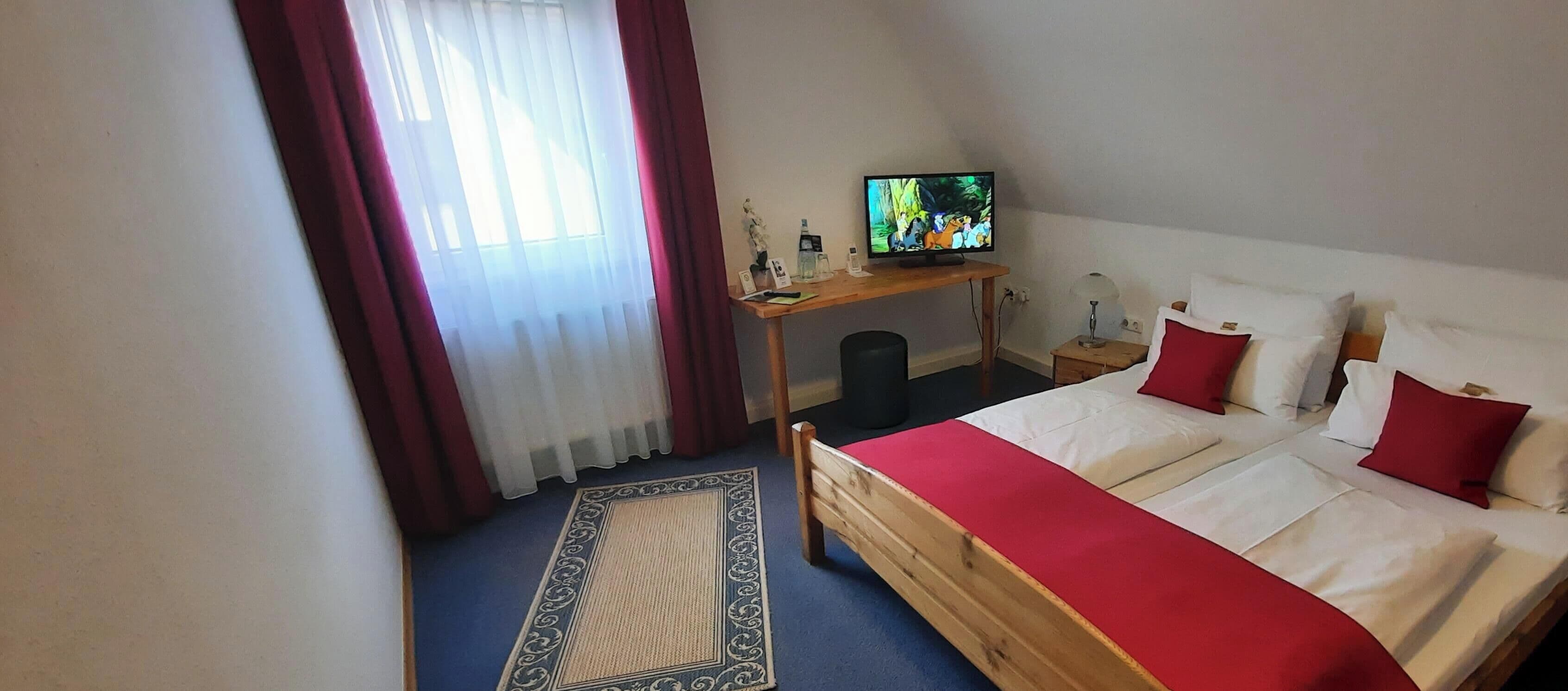 Een slaapkamer met een bed, een televisie, een bureau en een raam met gordijnen.