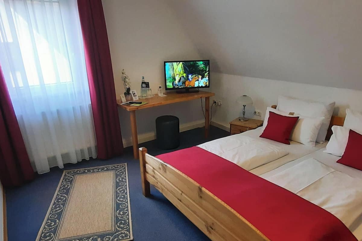 Een slaapkamer met een bed, een televisie, een bureau en een raam met gordijnen.
