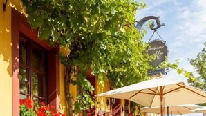 Un bâtiment jaune avec un mur couvert de lierre, une enseigne suspendue, des tables à l’extérieur et un chemin pavé.