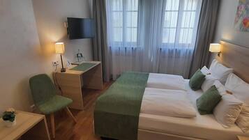 A hotel room with a bed, a desk, a chair, a TV, and a painting on the wall.