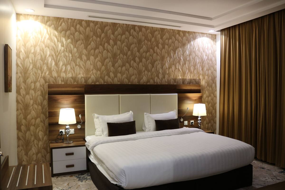 Une chambre d’hôtel avec un grand lit, deux tables de chevet avec des lampes, une tête de lit en bois et un papier peint à motifs.