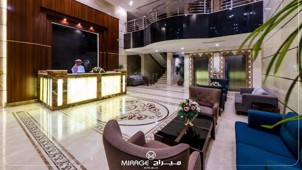 Een hotellobby met een receptiebalie, een zithoek en een trap naar een hoger niveau.