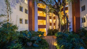 A multi-story building with a central courtyard, surrounded by lush greenery and a brick pathway. - Magnolia by Da Alohas El Arbol (Nerul)