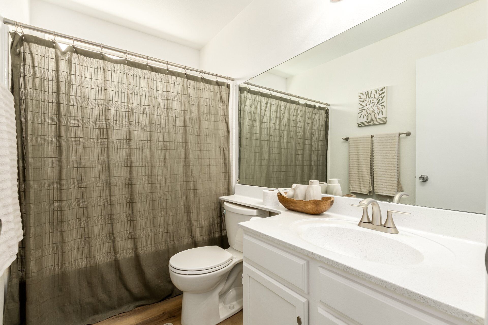A bathroom with a shower curtain, toilet, sink, and mirror.