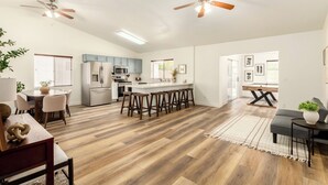 Une cuisine spacieuse dotée d’un îlot central, de planchers en bois et de ventilateurs de plafond.