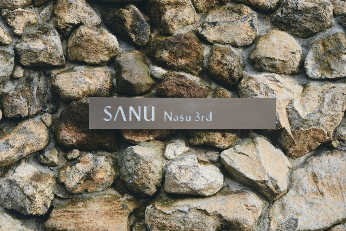 A stone wall with a sign that reads "SANU Nasu 3rd".