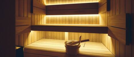 A sauna with wooden walls and benches, a bucket, and a wooden bench.