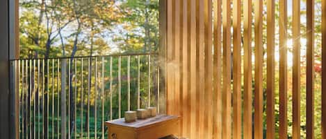 A wooden deck with a metal railing, a small wooden table with three objects, and a view of trees through the railing.