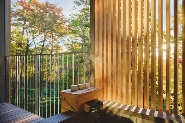 A wooden deck with a metal railing, a small wooden table with three objects, and a view of trees through the railing. - SANU 2nd Home Nasu 3rd (Nasu)