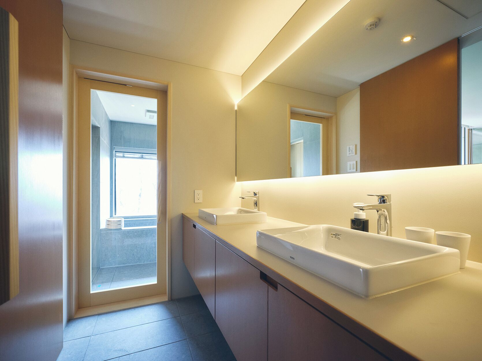 Un baño moderno con un espejo grande, dos lavamanos y una zona de ducha.